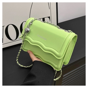 Detail of bright green crossbody bag with wavy flap design and silver chain strap