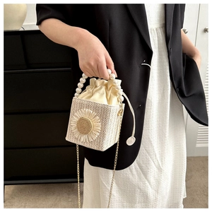 Detailed shot of beige woven bag with sunflower decor, pearl handle and drawstring pouch