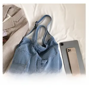 Adjustable strap detail and front pockets of a light blue denim tote bag for women
