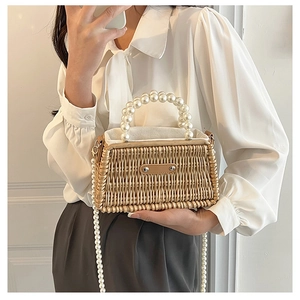 Detail of hand-woven straw bag featuring luxury pearl handle and elegant metal logo plate