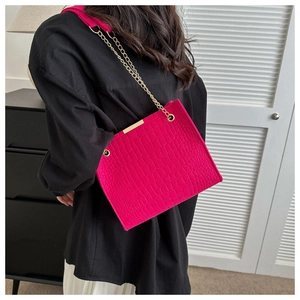 Detailed view of hot pink crocodile pattern bag with gold chain strap on female model