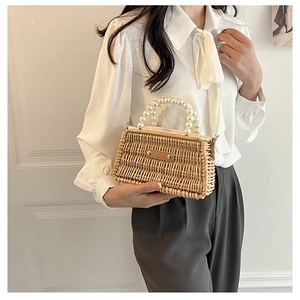 Detail of woven straw handbag featuring elegant pearl handle and leather patch detail