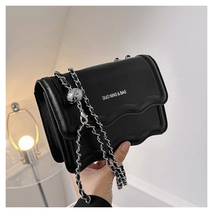 Detail of black leather bag with wavy edge, metal chain strap and adjustable silver ball