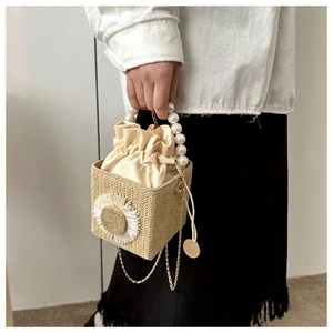 Detail of straw bucket bag with floral weave, pearl handle and golden chain strap