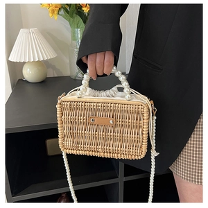 Close-up of woven straw box bag with large pearl handles and drawstring inner pouch