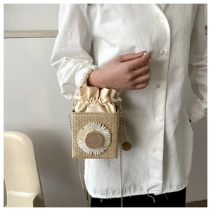 Detail of straw woven bucket bag with sunflower decor and pearl handle chain