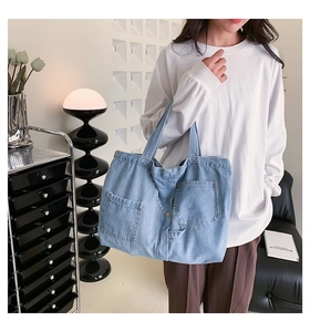 Macro detail of a light blue denim tote bag showing front pockets and texture