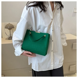 Detail of green crocodile embossed handbag with gold chain and top handle on model