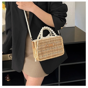 Detail of hand-woven straw bag featuring pearl handles and a cream drawstring liner