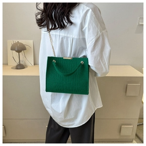 Detail of dark green crocodile texture tote bag with gold chain strap on model