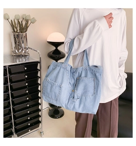 Detail of light blue denim tote bag with front pockets styled in a modern casual room