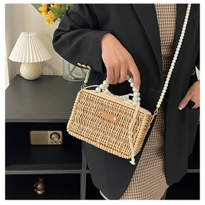 Detail of woven straw bag featuring large pearl handle and crossbody chain strap