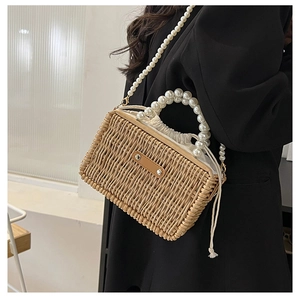 Detail of woven straw bag featuring elegant pearl top handle and drawstring lining