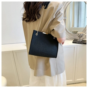 Detail of black crocodile pattern felt tote bag with gold chain and metal top trim