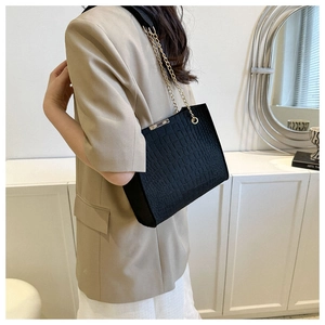 Detail of black crocodile texture tote bag featuring golden metal chain strap