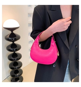 Detail of rose pink crocodile pattern crescent bag with gold hardware held by a model