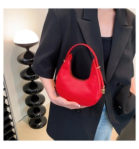 Detail of red croc-embossed crescent bag held by model in black blazer and jeans