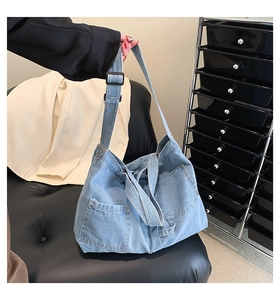 Close-up of light blue denim tote bag featuring external pocket and adjustable black strap