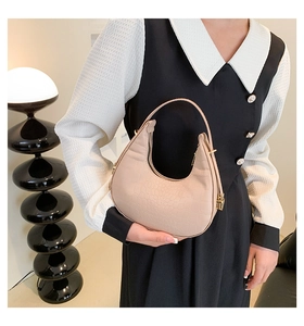 Detailed view of beige crocodile embossed hobo bag held by a model in a stylish dress