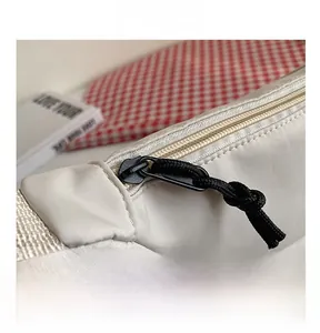 Détail du sac en nylon beige montrant la fermeture éclair noire et la tirette tressée