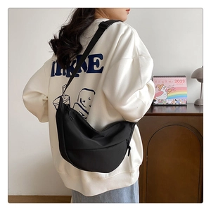 Gros plan d'un sac demi-lune en nylon noir porté à l'épaule dans un intérieur cosy