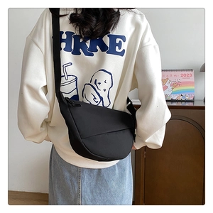 Gros plan du sac croissant en nylon noir porté en bandoulière sur un sweat blanc