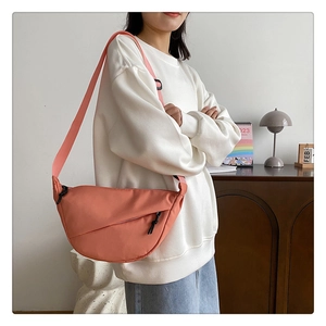 Gros plan d'un sac demi-lune en nylon rose corail avec bandoulière porté par un modèle