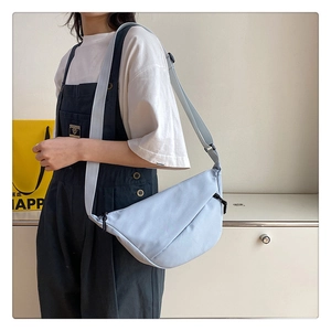 Gros plan d'un sac demi-lune en nylon bleu clair avec bandoulière porté par un mannequin