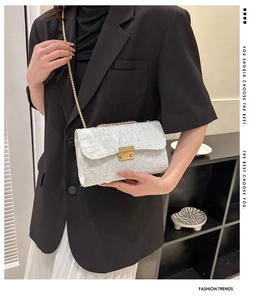 Detail of white pleated texture fabric with golden square lock and metal chain strap