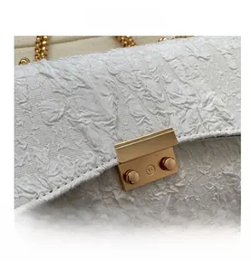 Macro view of white textured fabric bag featuring a gold clasp and metal chain link detail