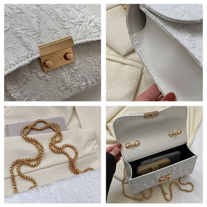 Detail view of white pleated oxford bag with golden buckle and chain shoulder strap
