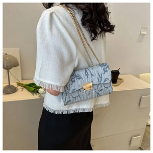 Detail of light blue wrinkled Oxford cloth crossbody bag with gold chain strap worn by model