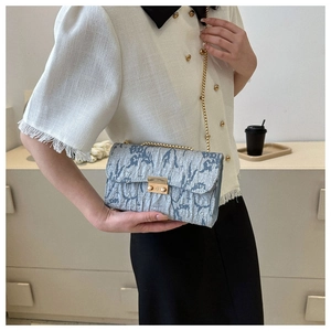 Detail of silver-blue pleated fabric handbag with gold chain strap and metal lock
