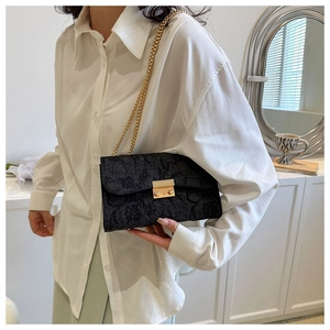 Detail of black textured crossbody bag with gold chain strap worn over a white shirt