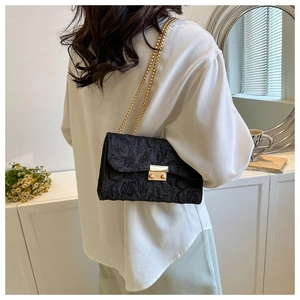 Detail of black textured crossbody bag with double gold chain straps and metal buckle