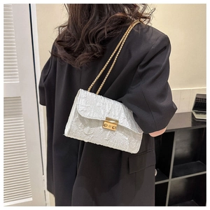 Detail of white pleated oxford crossbody bag with gold chain strap on model's black suit