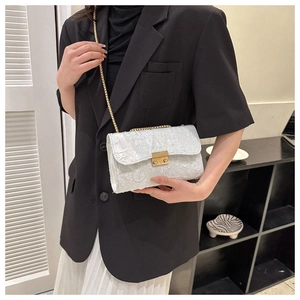Detail of white jacquard texture crossbody bag with gold chain strap and metal lock