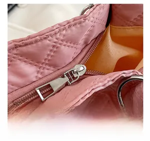 Detail shot of a smooth silver zipper on a pink quilted nylon tote with orange lining