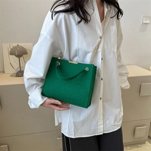 Dark green crocodile embossed tote bag with gold chain strap shown on a model