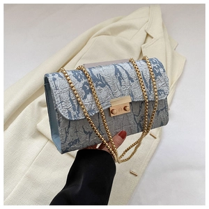 Detail of light blue textured fabric with gold metal chain and square buckle on handbag