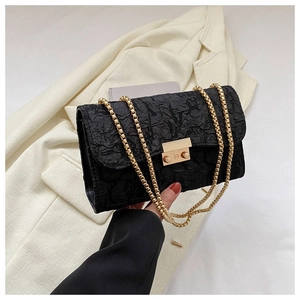 Detail of black pleated fabric bag featuring a gold metal clasp and chain shoulder strap