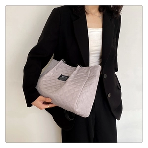 Close-up of light grey quilted tote bag with fashion label shown on a minimalist model