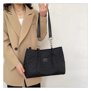 Detail of black quilted nylon tote bag with silver chain strap and fashion label