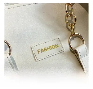Close-up of elegant beige tote bag featuring golden chain handle and fashion logo engraving
