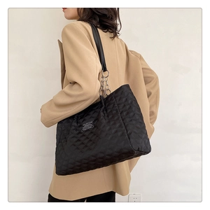 Detailed view of black quilted nylon tote bag with chain strap on a model's shoulder