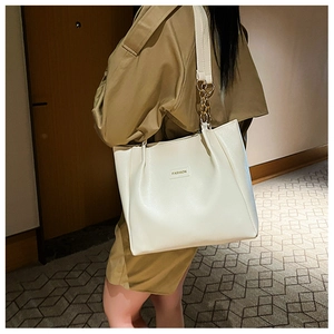 Detail of white tote bag featuring metal chain shoulder strap and FASHION logo tag
