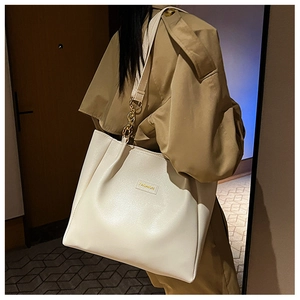 Close-up of beige leather tote bag featuring gold chain straps and fashion emblem