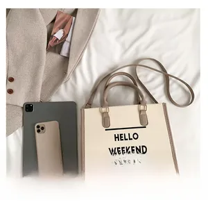 Vue de dessus du sac cabas beige avec texte HELLO WEEKEND et lanières marron sur lit