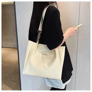 Detail of cream leather tote bag with gold chain strap and fashion label on the front