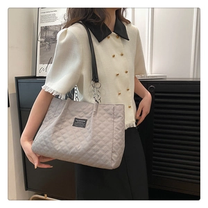 Detail of grey quilted nylon tote bag with fashion logo and chain strap on shoulder